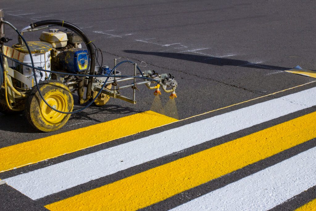 a man is painting a yellow and white stripe on a road.